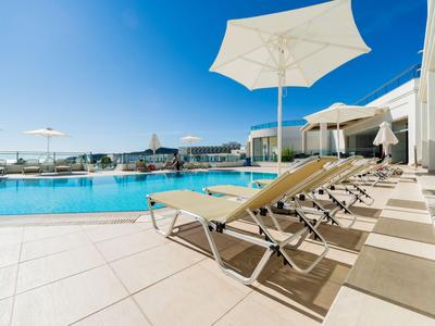 Reihen von Liegestühlen und Sonnenschirmen neben einem großen Außenpool bei klarem Himmel.