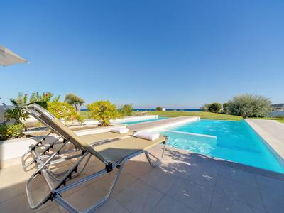 Zwei Liegestühle neben einem Pool mit Blick auf den Garten und den klaren Himmel.
