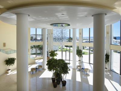 Heller Hotellobby mit großen Fenstern, Pflanzen und Ausblick auf Außenbereich