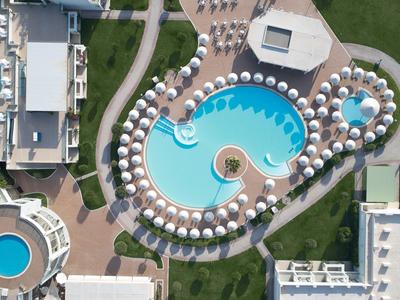 Luftaufnahme eines Hotelkomplexes mit mehreren Schwimmbädern und Sonnenschirmen.