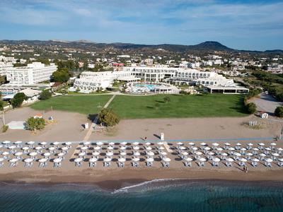 Toma aérea de un complejo hotelero en la playa con filas de sombrillas y tumbonas.
