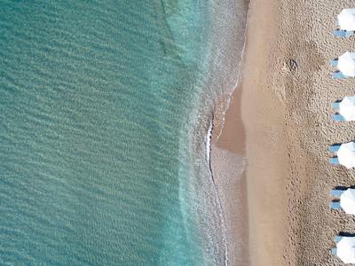 Vista aérea de una playa con filas de sombrillas blancas junto a agua azul clara.