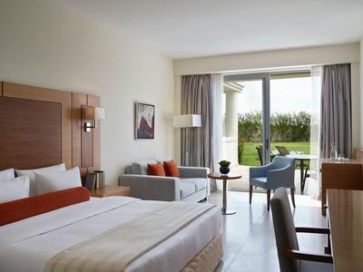 Habitación de hotel moderna con cama doble, sofá y acceso a terraza con vistas al jardín.