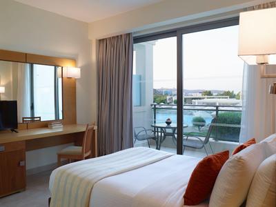 Habitación de hotel con cama doble, escritorio y balcón con vista al agua y muebles exteriores.