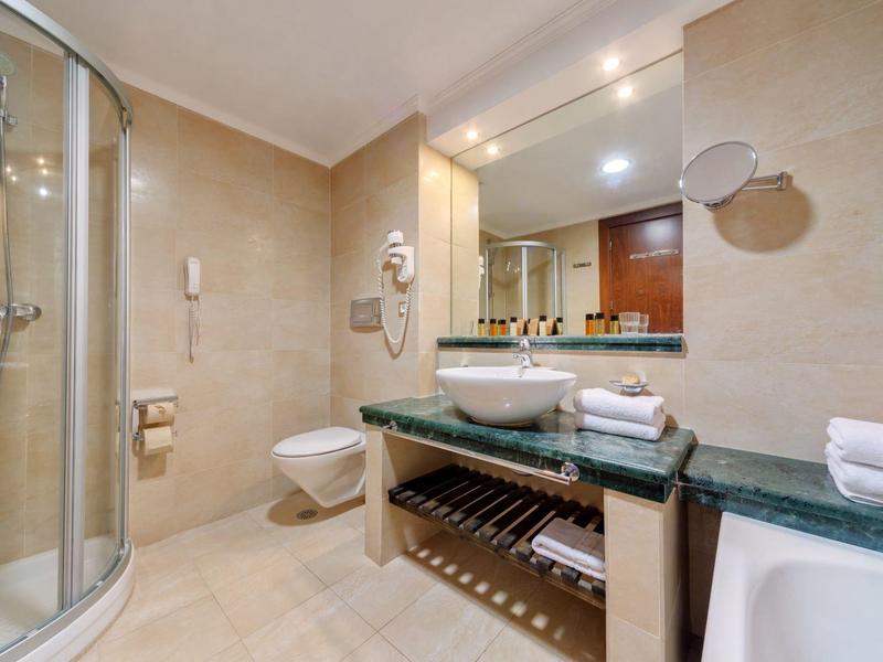 Baño de hotel con ducha de vidrio, inodoro, lavabo y toallas sobre encimera de mármol.