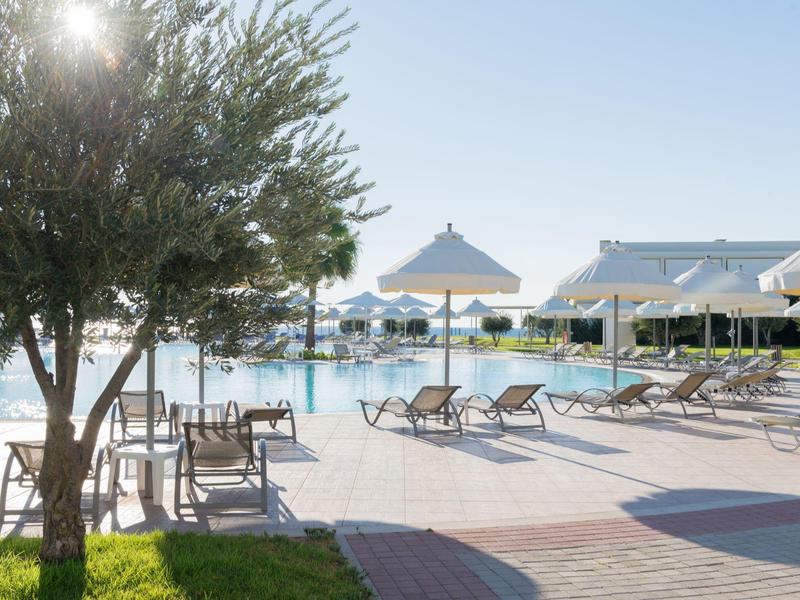 Área soleada de piscina con sillas, tumbonas y sombrillas junto a vista al mar.