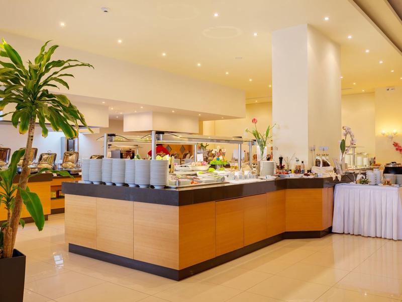 Área de buffet en un restaurante de hotel luminoso con plantas y decoración moderna.