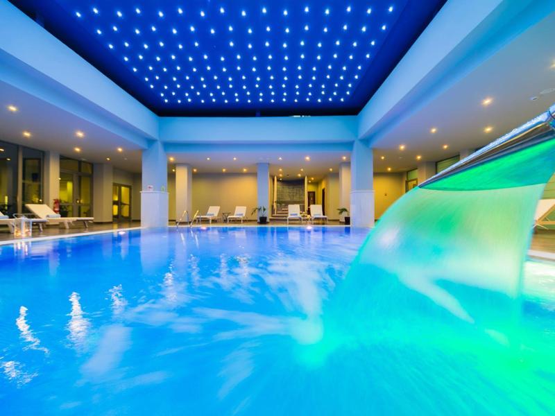 Piscina interior bien iluminada con cascada y tumbonas en un hotel