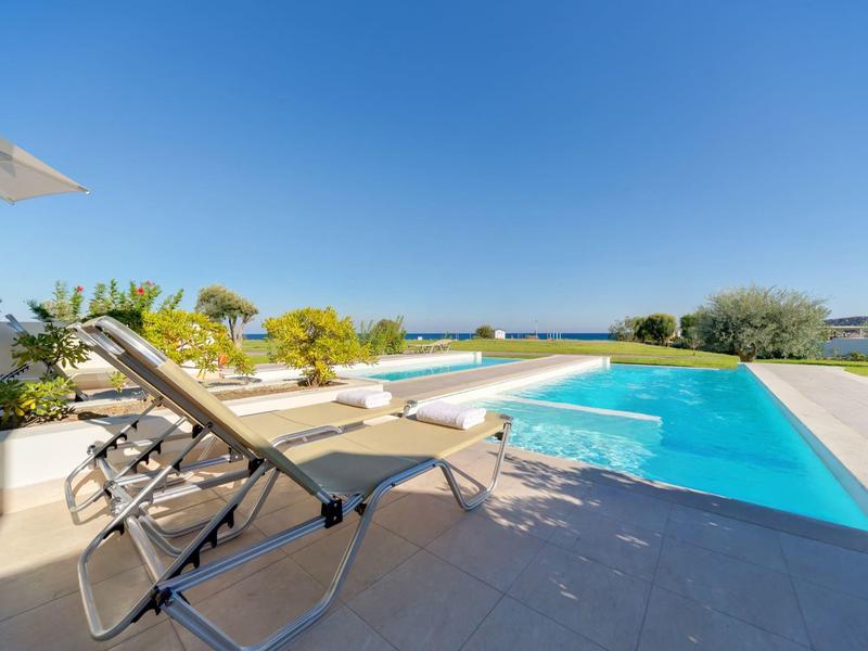 Piscina moderna con dos tumbonas y cielo azul claro de fondo.