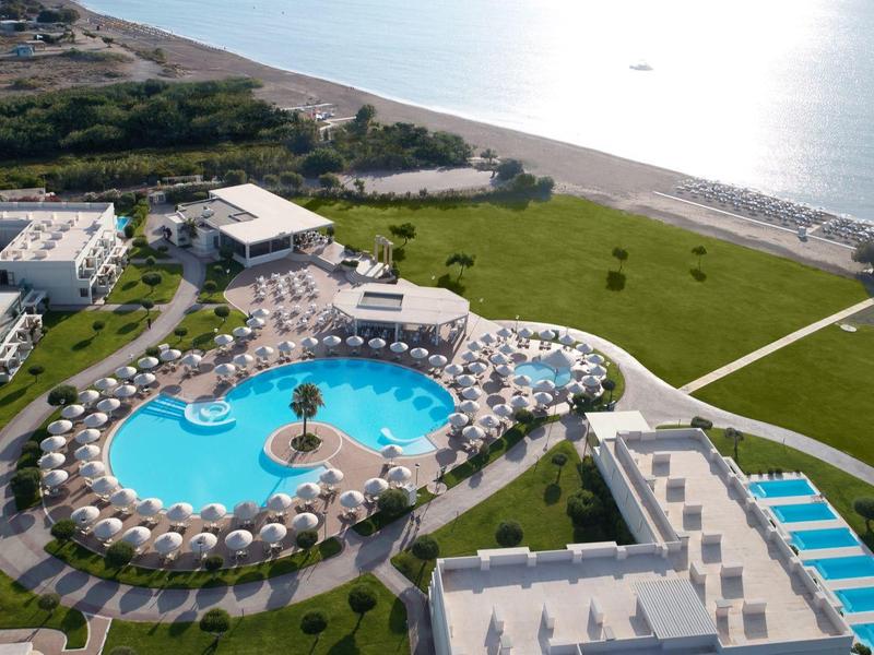 Vista de un hotel con gran piscina, tumbonas, playa y vista al mar en un día soleado