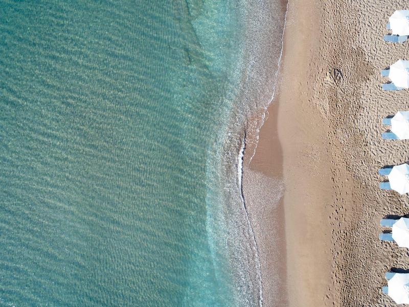 Vista aérea de una playa con filas de sombrillas blancas junto a agua azul clara.