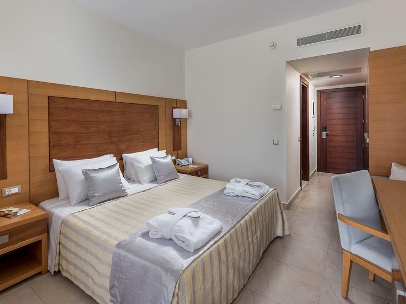 Habitación de hotel moderna con cama doble, muebles de madera y escritorio en tonos neutros.