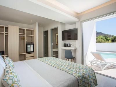 Nowoczesny pokój hotelowy z łóżkiem king-size, otwartą szafą i dostępem do tarasu z widokiem na basen.