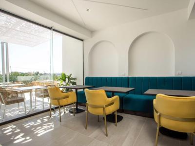 Nowoczesna część wypoczynkowa z żółtymi krzesłami i niebieskimi sofami obok dużej szklanej ściany z widokiem na zewnątrz.