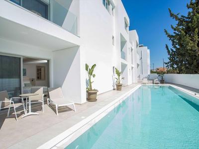 Nowoczesny basen hotelowy z białymi budynkami i miejscami do siedzenia na tarasie pod niebieskim niebem.