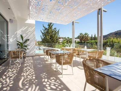 Słoneczny taras z nowoczesnymi wiklinowymi krzesłami, stolikami i dekoracyjnym zadaszeniem.