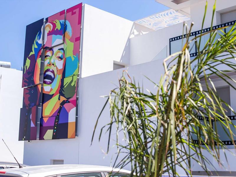 Kolorowy mural Marilyn Monroe na białej ścianie hotelu z zieloną palmą na pierwszym planie