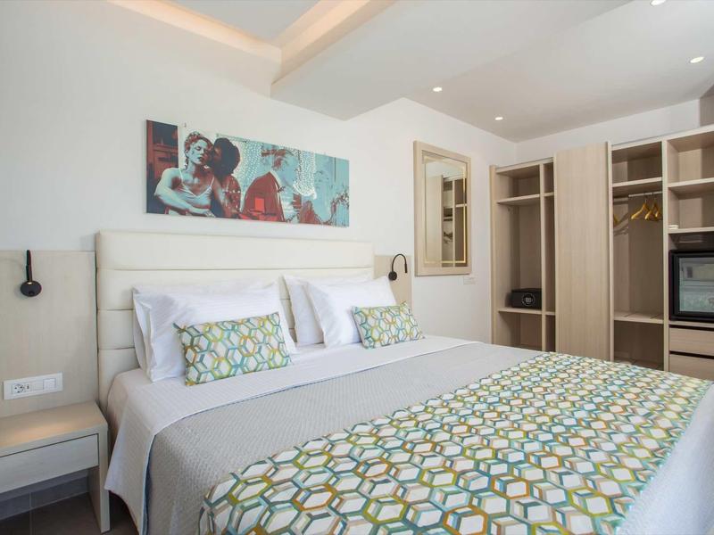 Nowoczesny pokój hotelowy z łóżkiem podwójnym, kolorową narzutą i przestronną szafą.