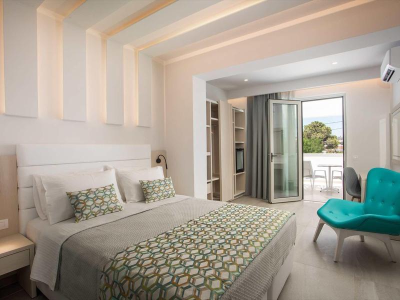 Nowoczesna sypialnia z podwójnym łóżkiem, turkusowym fotelem i dostępem do balkonu z widokiem na zewnątrz.