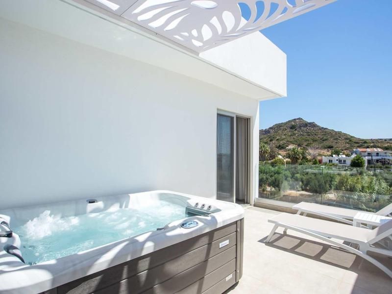 Nowoczesny balkon z jacuzzi i dwoma leżakami z widokiem na słoneczne góry.