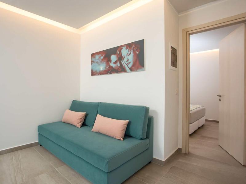 Nowocześnie urządzone pomieszczenie z zieloną sofą, poduszkami dekoracyjnymi i widokiem na sypialnię.