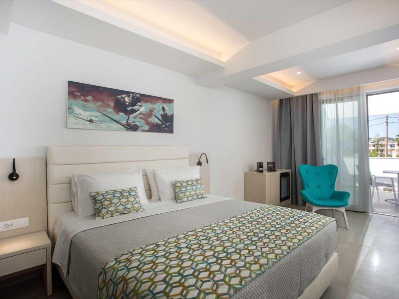 Nowoczesny pokój hotelowy z łóżkiem podwójnym, niebieskim fotelem i balkonem z widokiem na morze.