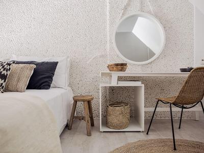 Camera luminosa con parete bianca, specchio rotondo, scrivania e sedia in vimini.