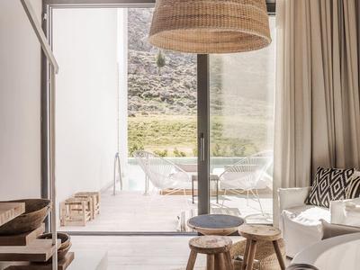 Lichte, gezellige woonruimte met rotan hanglamp, vloerkleed en uitzicht op terras en berglandschap.