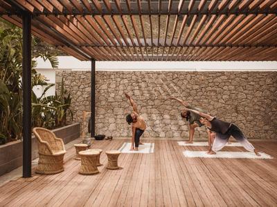 Tre persone fanno yoga in un'area esterna coperta con pavimento in legno e sedie.