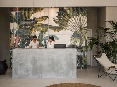 Hotelreceptiebalie met twee medewerkers en tropische wanddecoratie.