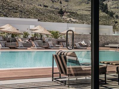 Area piscina moderna con lettini e ombrelloni davanti a uno sfondo montano.