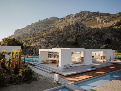 Edificio bianco moderno con piscina davanti a una montagna rocciosa sotto un cielo limpido.
