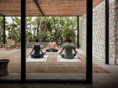 Tre persone fanno yoga su pavimento in legno di fronte a un giardino tropicale in uno spazio aperto.
