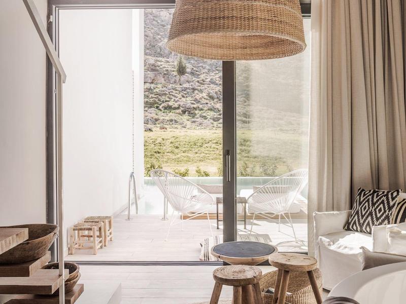 Lichte, gezellige woonruimte met rotan hanglamp, vloerkleed en uitzicht op terras en berglandschap.