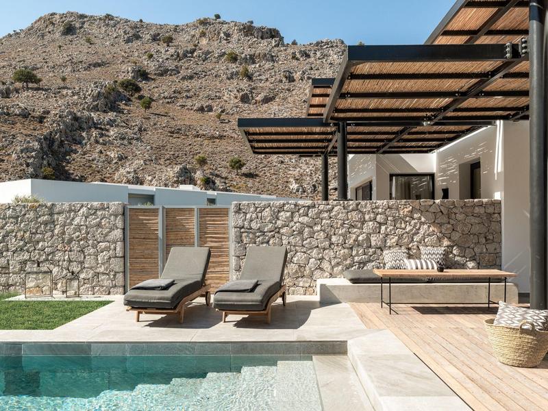 Moderne buitenruimte met zwembad, ligstoelen, eettafel en stenen muur voor bergen.