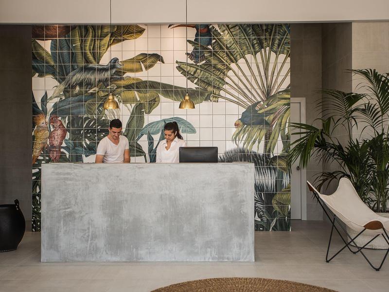 Hotelreceptiebalie met twee medewerkers en tropische wanddecoratie.