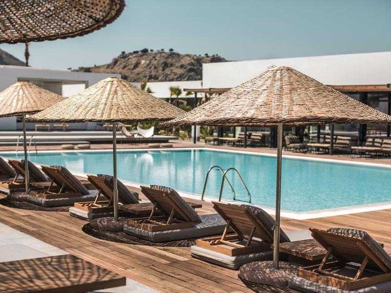 Zwembadgedeelte met ligstoelen en parasols van riet op een houten terras.