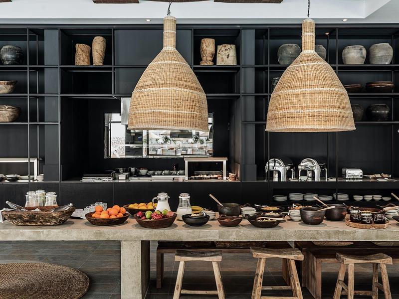 Moderne keuken met houten krukken, zwarte planken en grote geweven hanglampen.