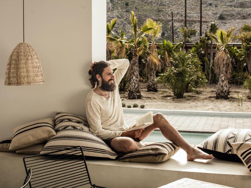 Man ontspant op een buitenzit met kussens naast zwembad en tuin.