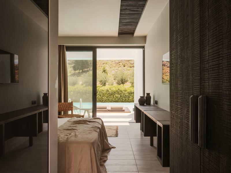 Slaapkamer met open deuren naar terras en uitzicht op tuin en natuur.