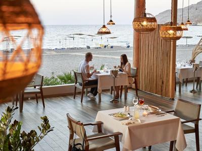 Restaurantterrasse am Strand mit gedeckten Tischen und Gästen bei Sonnenuntergang.