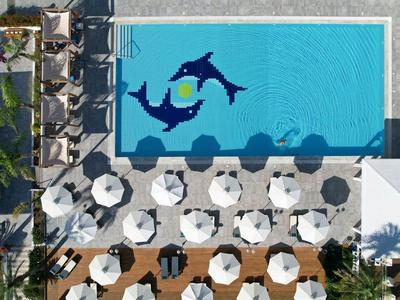 Vogelperspektive eines Pools mit Delfinmosaik und weißen Sonnenschirmen auf der Terrasse.