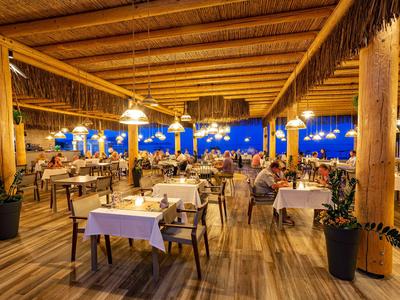 Freiluftrestaurant mit Holzdecke und Tischen bei Dämmerung mit Blick auf das Meer.