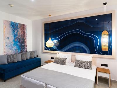 Chambre d'hôtel moderne avec grand lit double, canapé bleu et art mural abstrait.