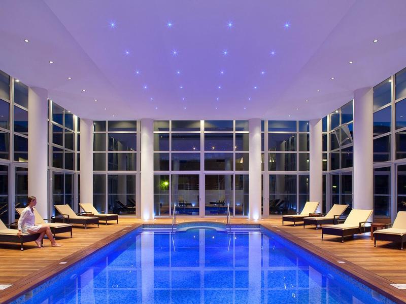 Piscine intérieure avec éclairage bleu et chaises longues dans un salon moderne