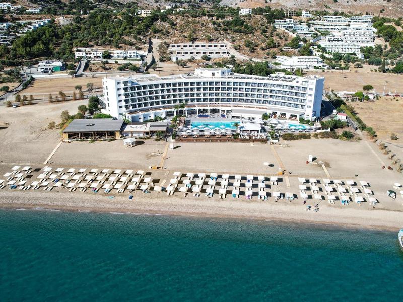 Grand hôtel avec piscine et transats sur la plage au bord d'une eau claire et bleue.