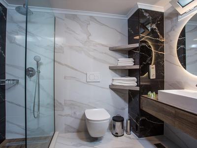 Nowoczesna łazienka z szklaną kabiną prysznicową, wiszącą toaletą i okrągłym podświetlanym lustrem.