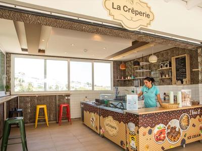 Jasna kawiarnia z kolorowymi stołkami i dużym ladą w ciepłych barwach.