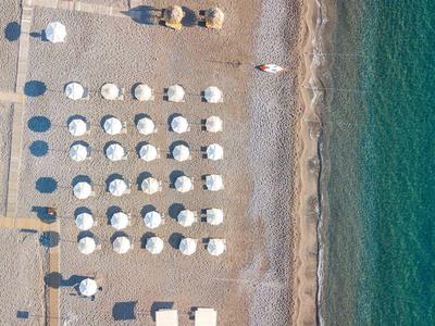 Widok z lotu ptaka na plażę z rzędami parasoli i niebieską wodą.