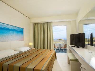 Nowoczesny pokój hotelowy z łóżkiem podwójnym, telewizorem i balkonem z widokiem na morze.